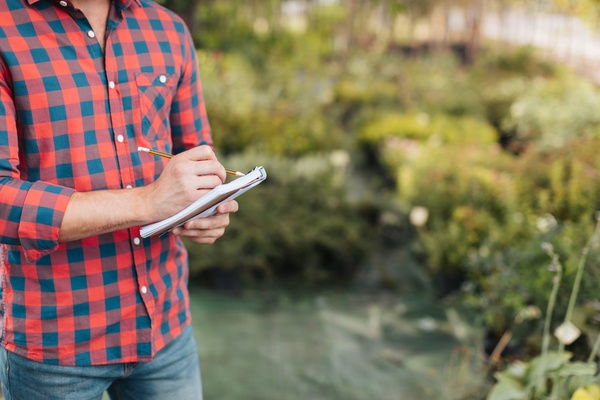 Gardener making notes in notebook while standing in garden