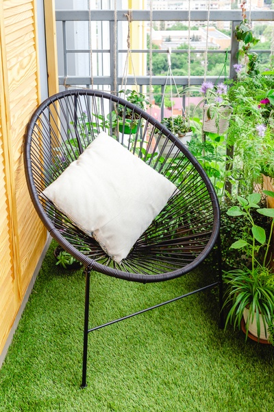 Garden chair with pillow on balcony at home in appartment on lawn grass with house plants flowers. Garden veranda modern terrace.