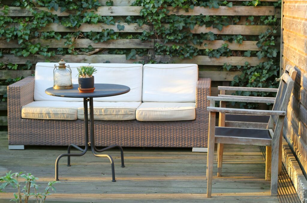 Modern garden architecture with relax corner, a wicker bench with pillows and a grey wooden floor