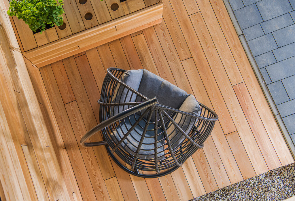 An egg chair swing hanging  over a warm wooden decked area in the garden